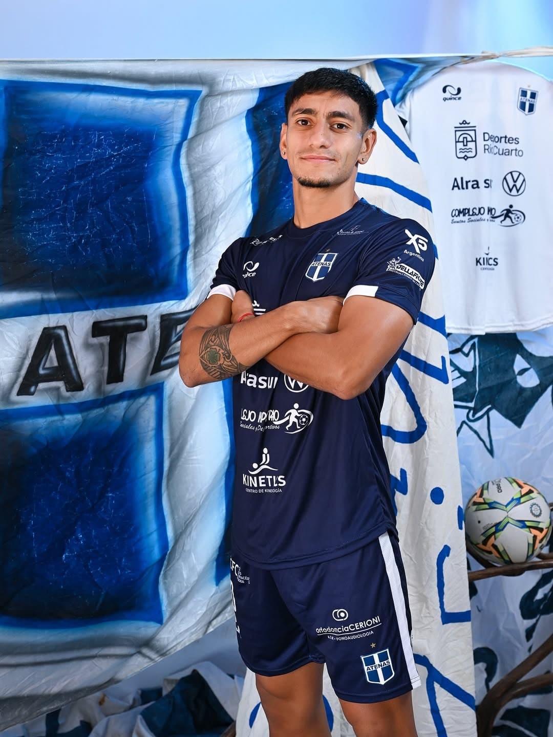 Fotografía promocional de un joven jugador de fútbol del Club Sportivo Biblioteca Atenas de Río Cuarto. Viste el uniforme alternativo azul oscuro de la temporada 2026, fabricado por la marca 'Quince'.